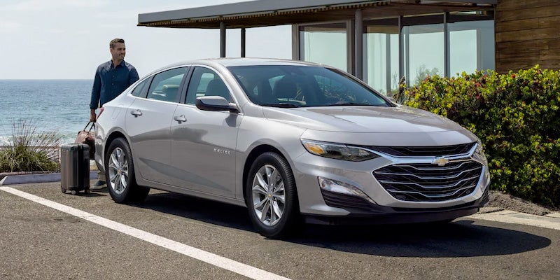 silver 2022 Chevrolet Malibu parked at house with man standing behind loading suticase
