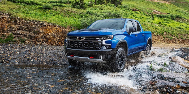 Blue 2022 Chevrolet Silverado 1500 driving in shallow rocky stream