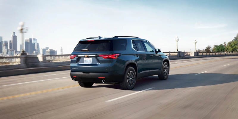 rear angled view of 2022 Chevrolet Traverse driving on highway with city in background