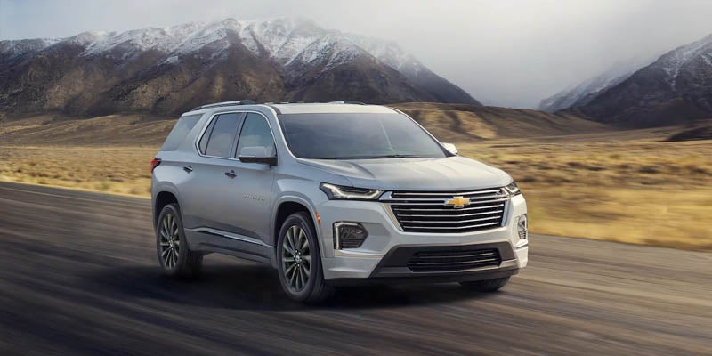 White 2022 Chevrolet Traverse driving on road with snowcapped mountains behind