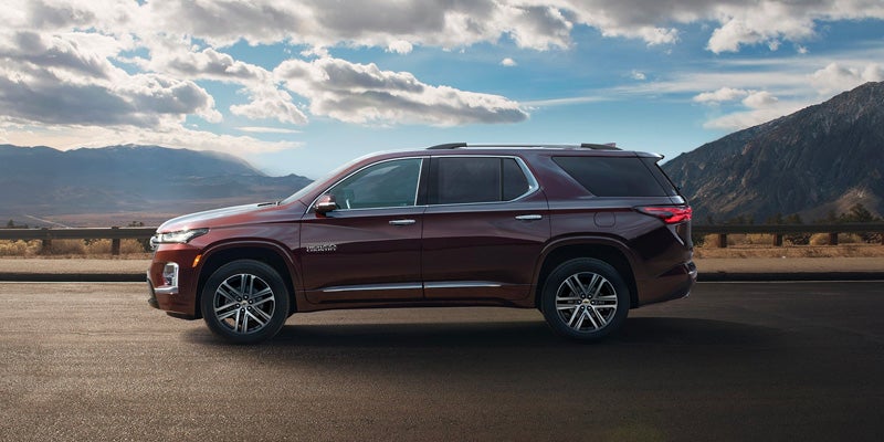 Side view of a red 2023 Chevrolet Traverse parked on road with mountains behind