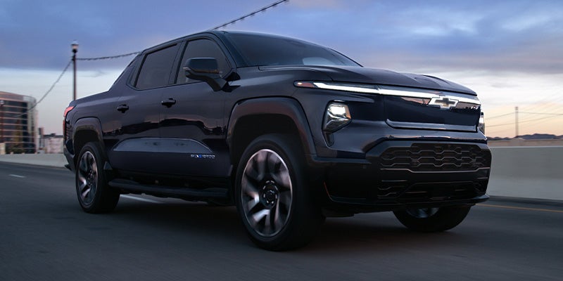 Black 2024 Chevrolet Silverado EV driving with headlights on
