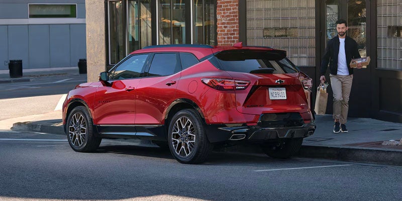 Red 2025 Chevrolet Blazer parked on street in a town, man walking toward car with grocery bag